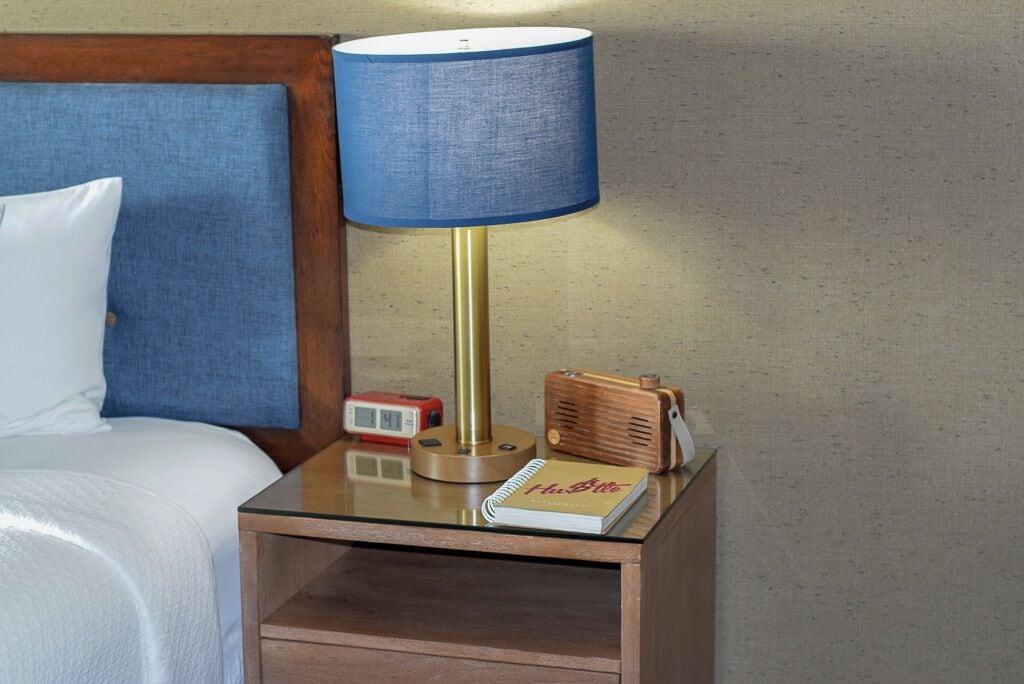 Une table de chevet avec une lampe, un livre, une radio et une horloge.