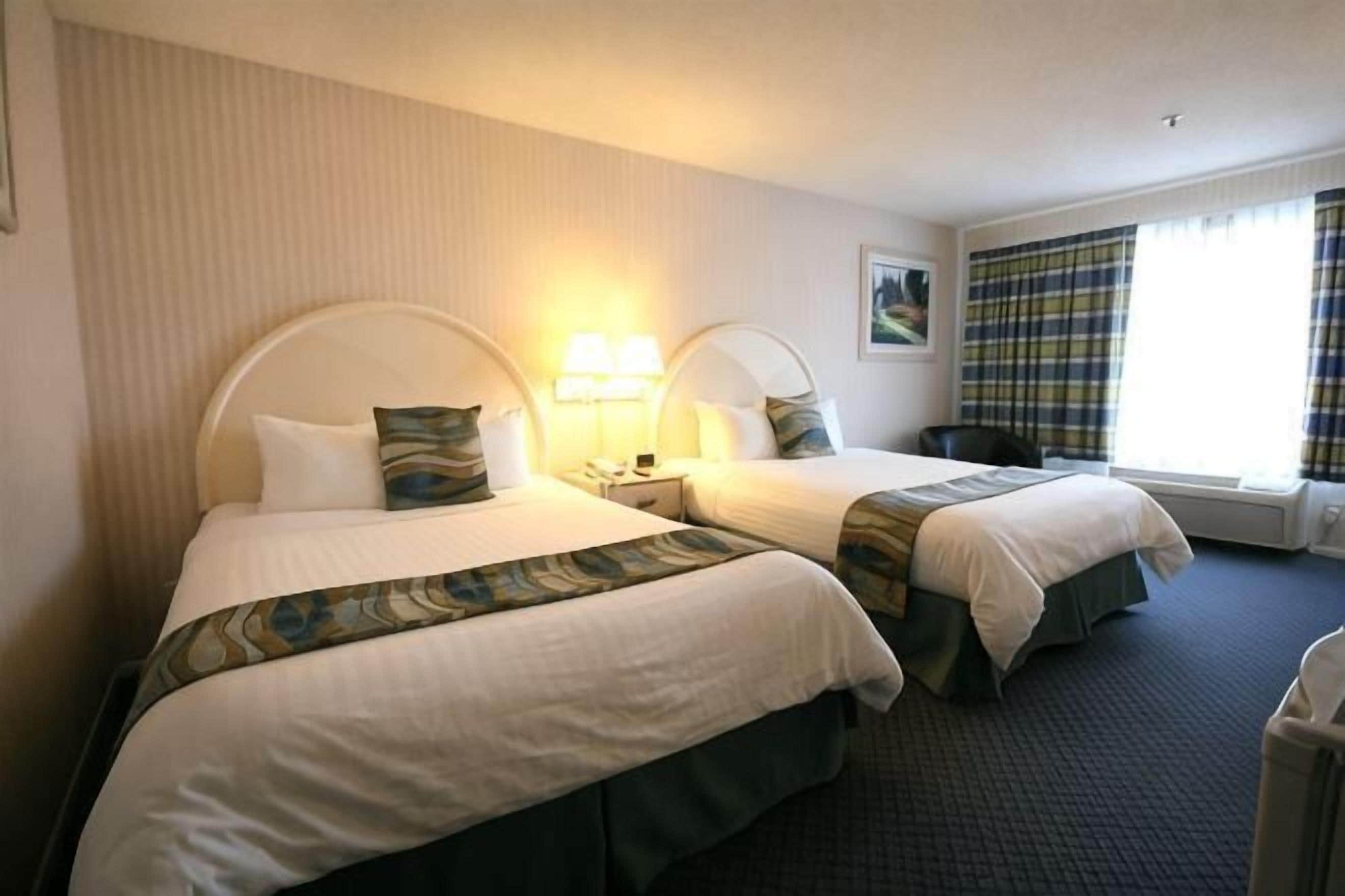 Ein Hotelzimmer mit zwei Betten, einem Nachttisch, einem Stuhl und einem Fenster mit Vorhängen.