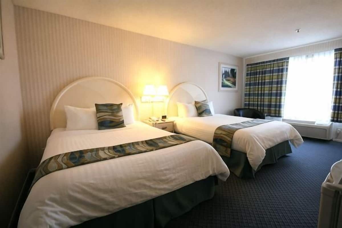 Ein Hotelzimmer mit zwei Betten, einem Nachttisch, einem Stuhl und einem Fenster mit Vorhängen.