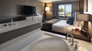 A modern hotel room with a large bed, a flat-screen TV, a large window with a view, a bathroom with a bathtub, and a desk with a lamp. - Hotel Hermosa (Hermosa Beach)
