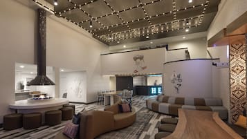 A modern hotel lobby with a central seating area, a bar, and a reception desk.