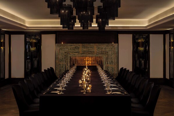 A long dining table with chairs, candles, and a chandelier in a dimly lit room with a patterned wall and a fireplace. - The May Fair Hotel, Mayfair London (London)