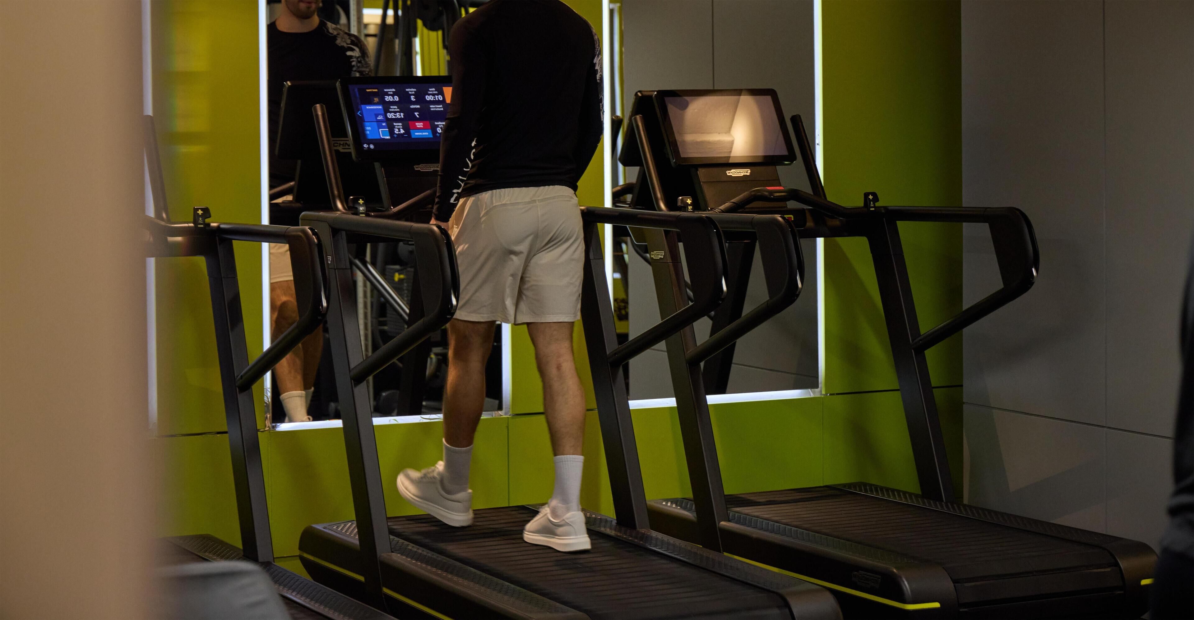 A person using a treadmill in a gym with a digital display and a mirror.