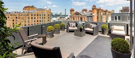 Terraza en la azotea con muebles de mimbre, plantas en macetas y vistas a la ciudad.