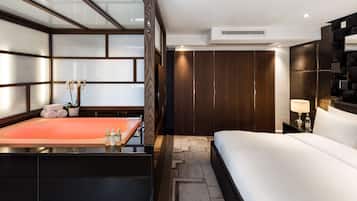 Ein modernes Hotelzimmer mit einem großen Bett, einem in Glas eingefassten Duschbereich, einem Holzschrank und einem Nachttisch mit Lampe.