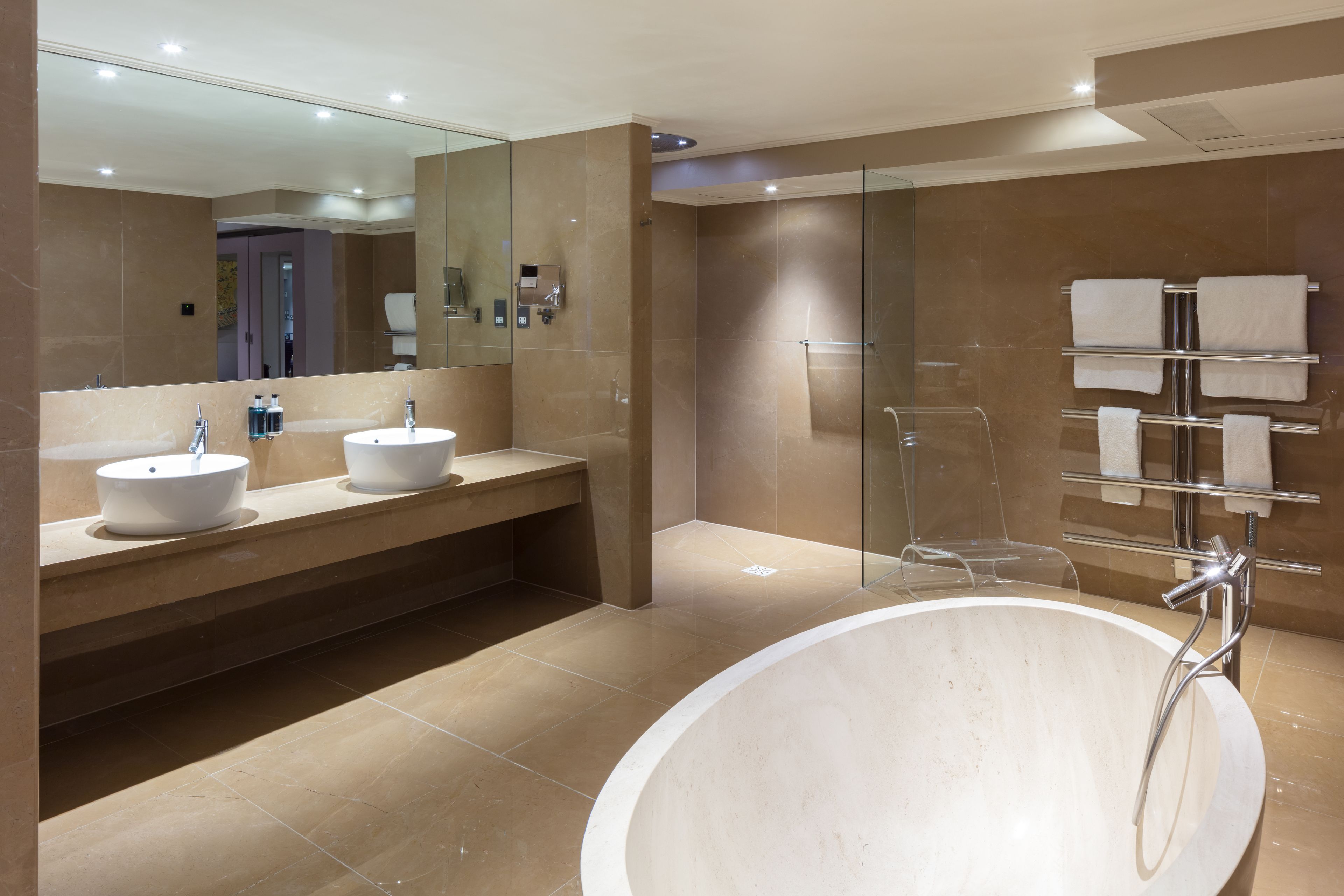 A modern bathroom with a large bathtub, two sinks, a glass shower enclosure, and a towel rack.