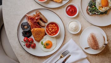 A breakfast spread with eggs, bacon, sausages, toast, beans, and a cup of coffee on a table.