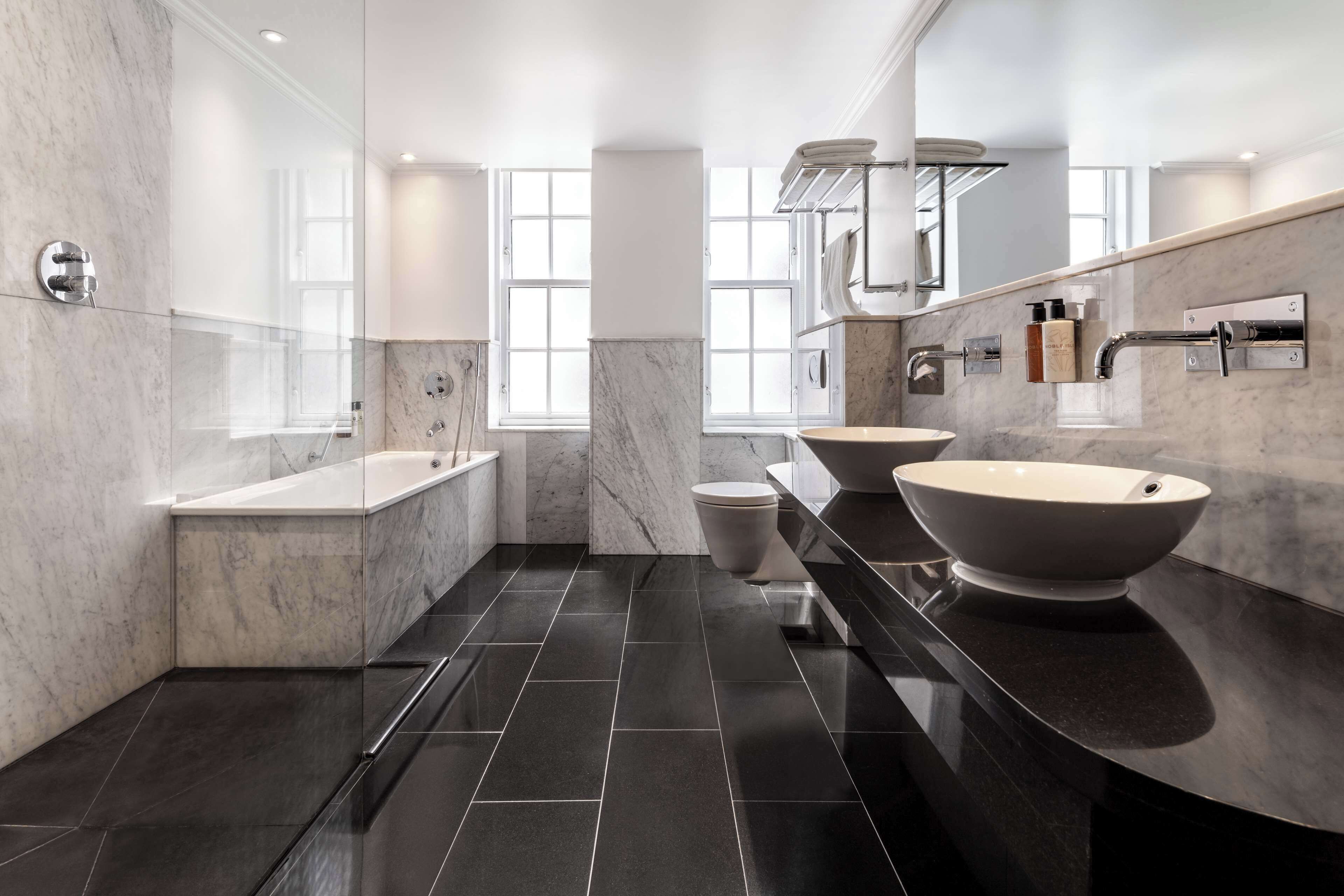 A modern bathroom with two sinks, a bathtub, and a toilet.