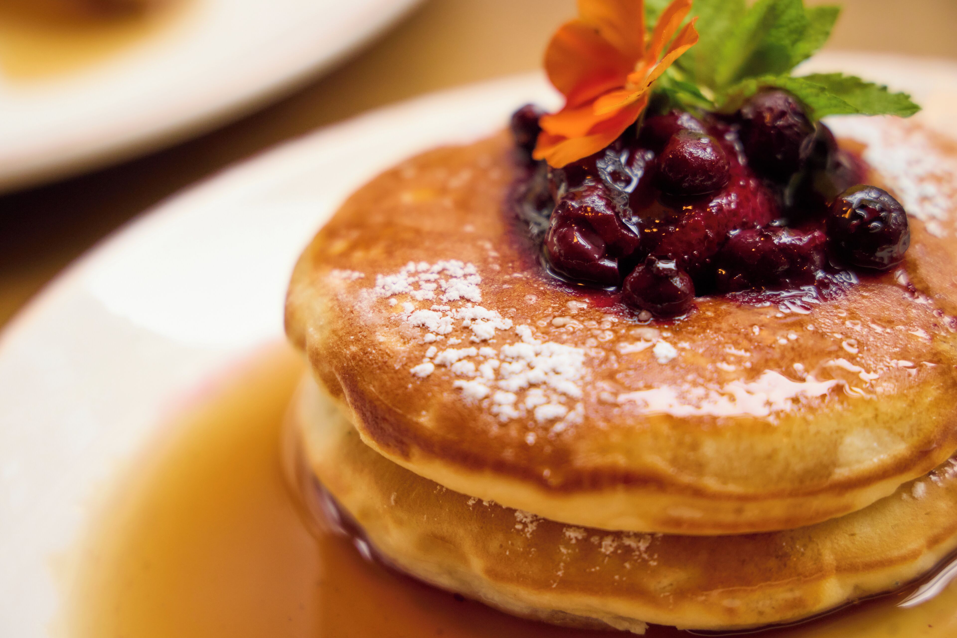 A stack of pancakes with syrup and a berry compote on top, garnished with a flower.