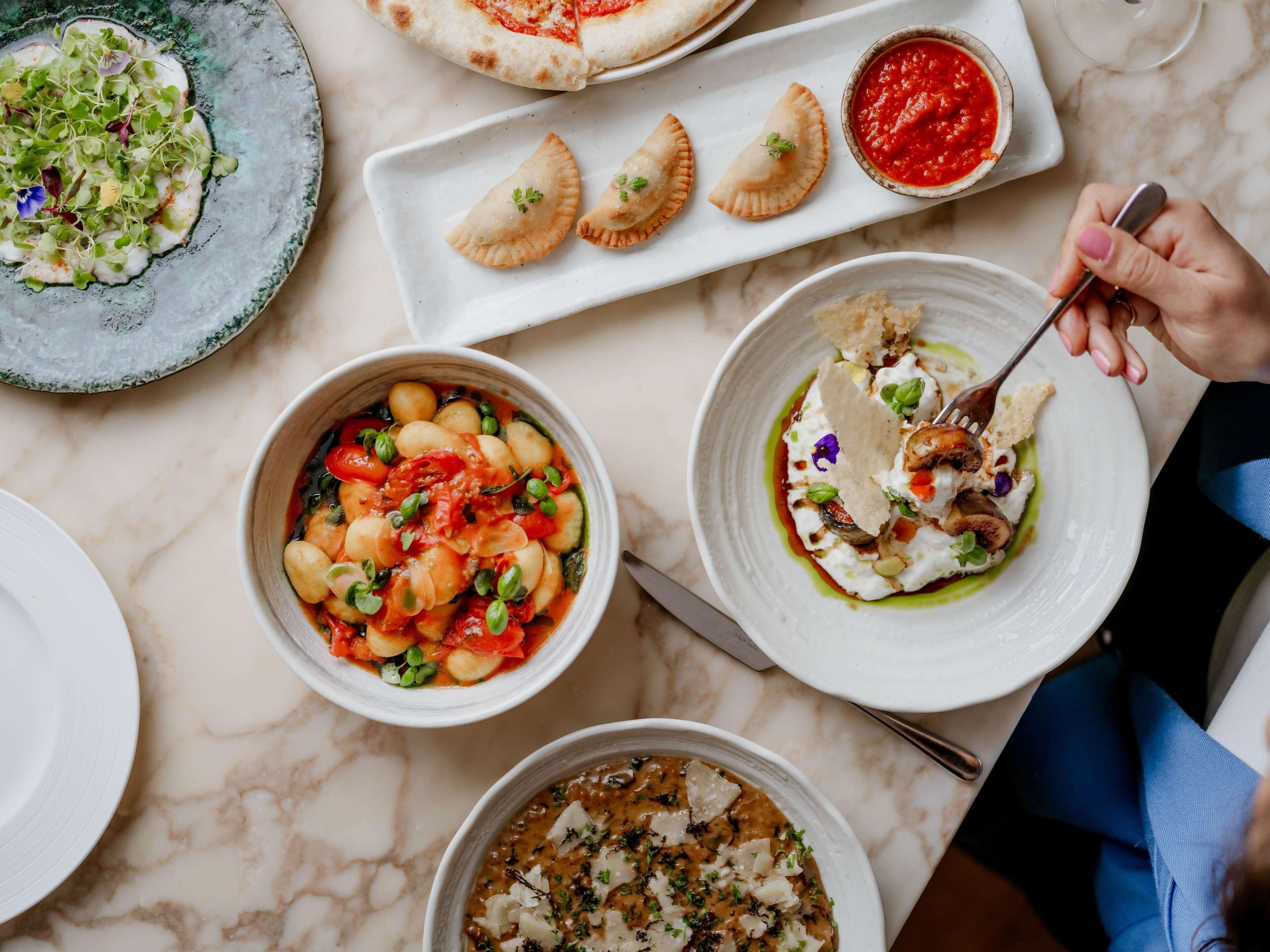 A variety of dishes on a marble table, including pasta, a pizza, and a bowl of soup.