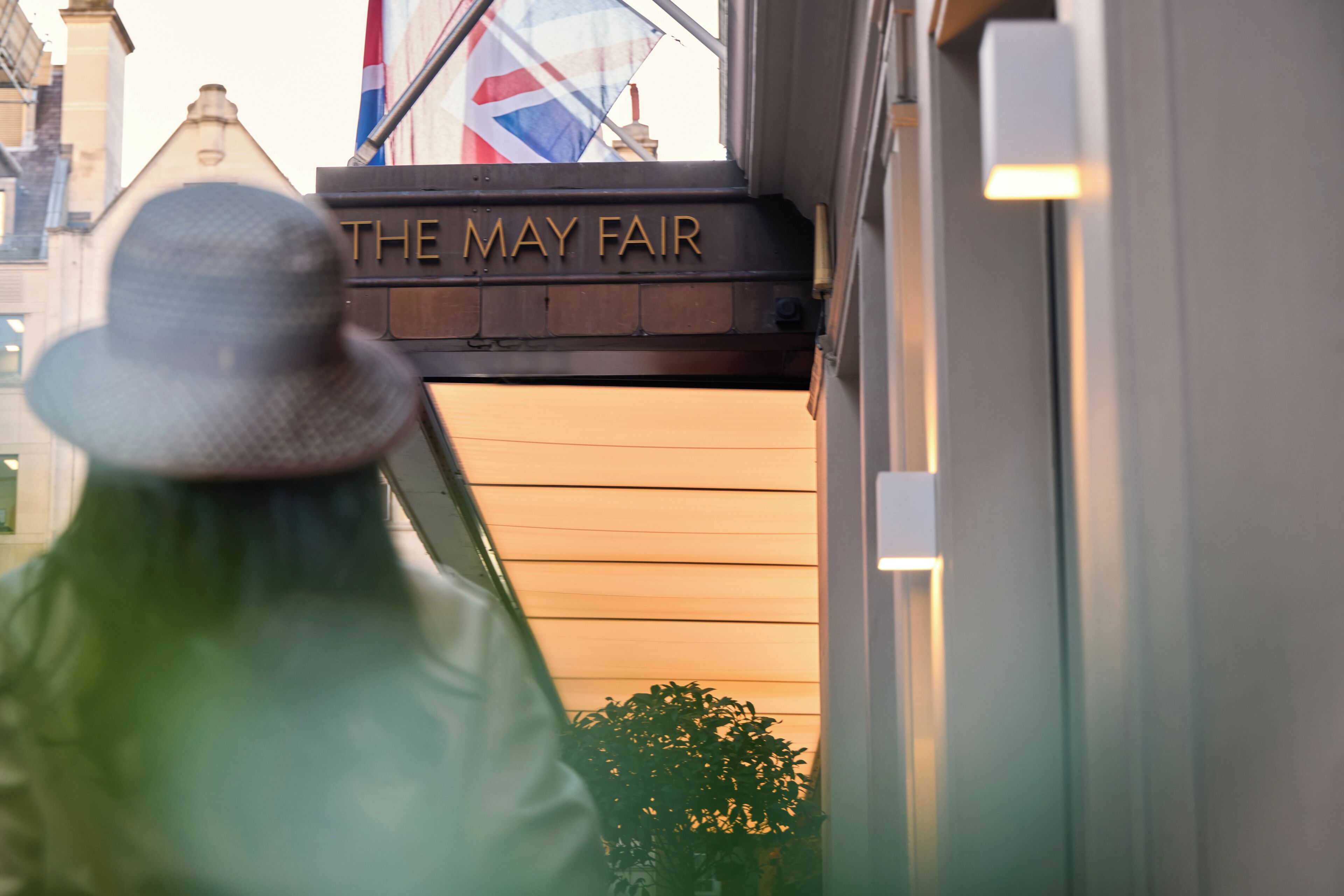 A building entrance with a sign reading 'THE MAY FAIR' and a flag in the background.