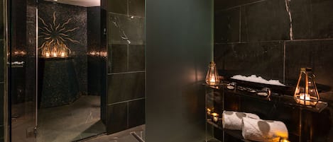 A modern bathroom with a glass shower enclosure, a decorative wall feature, and a shelf with toiletries and candles.