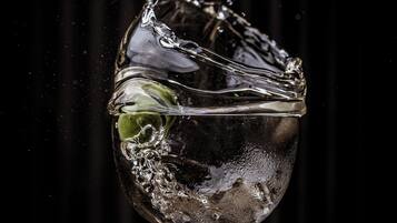 Un bicchiere d'acqua con un oggetto verde all'interno, che schizza su uno sfondo scuro.