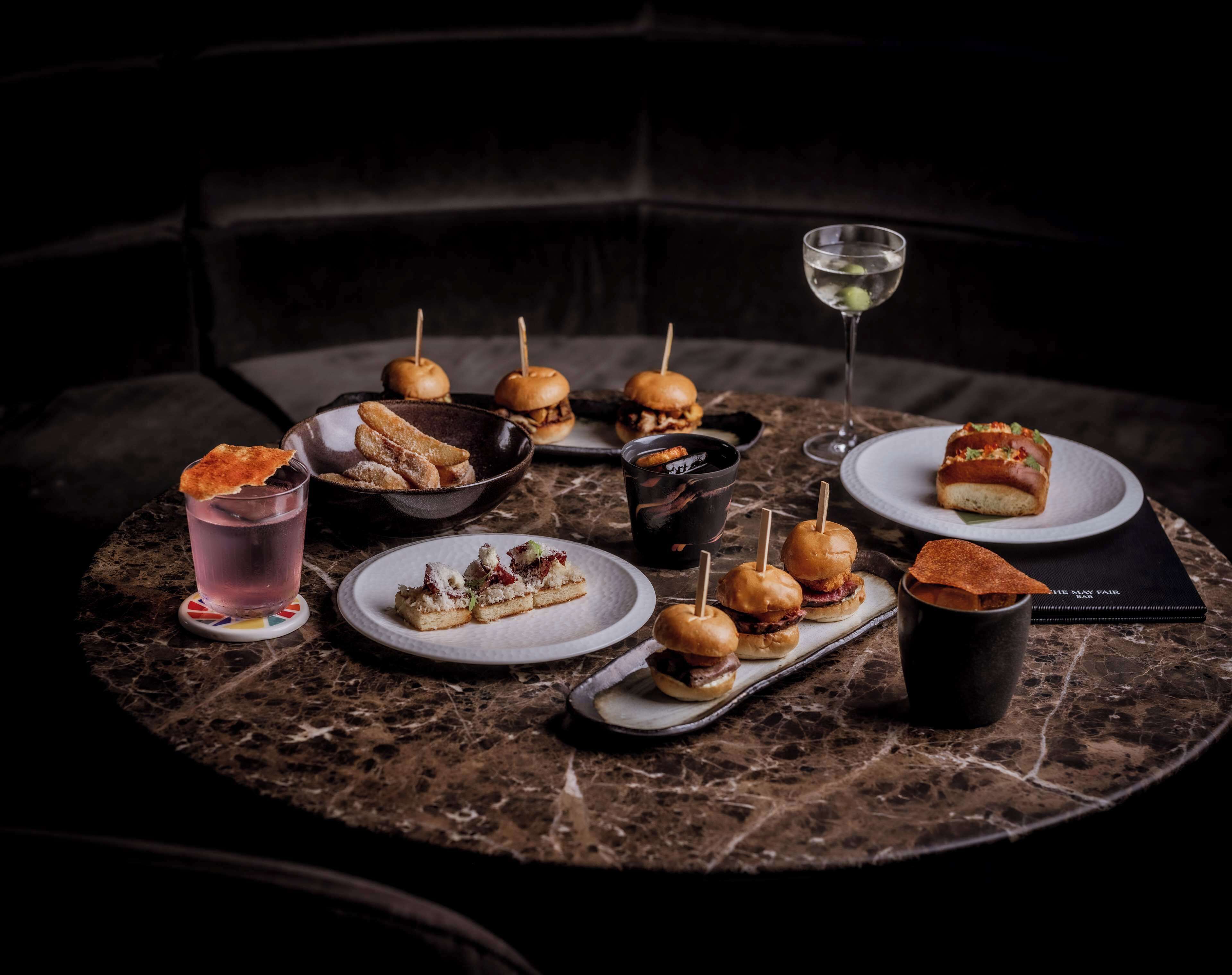 A marble table with various food items and drinks, including sandwiches, a drink with a garnish, and a glass of water.