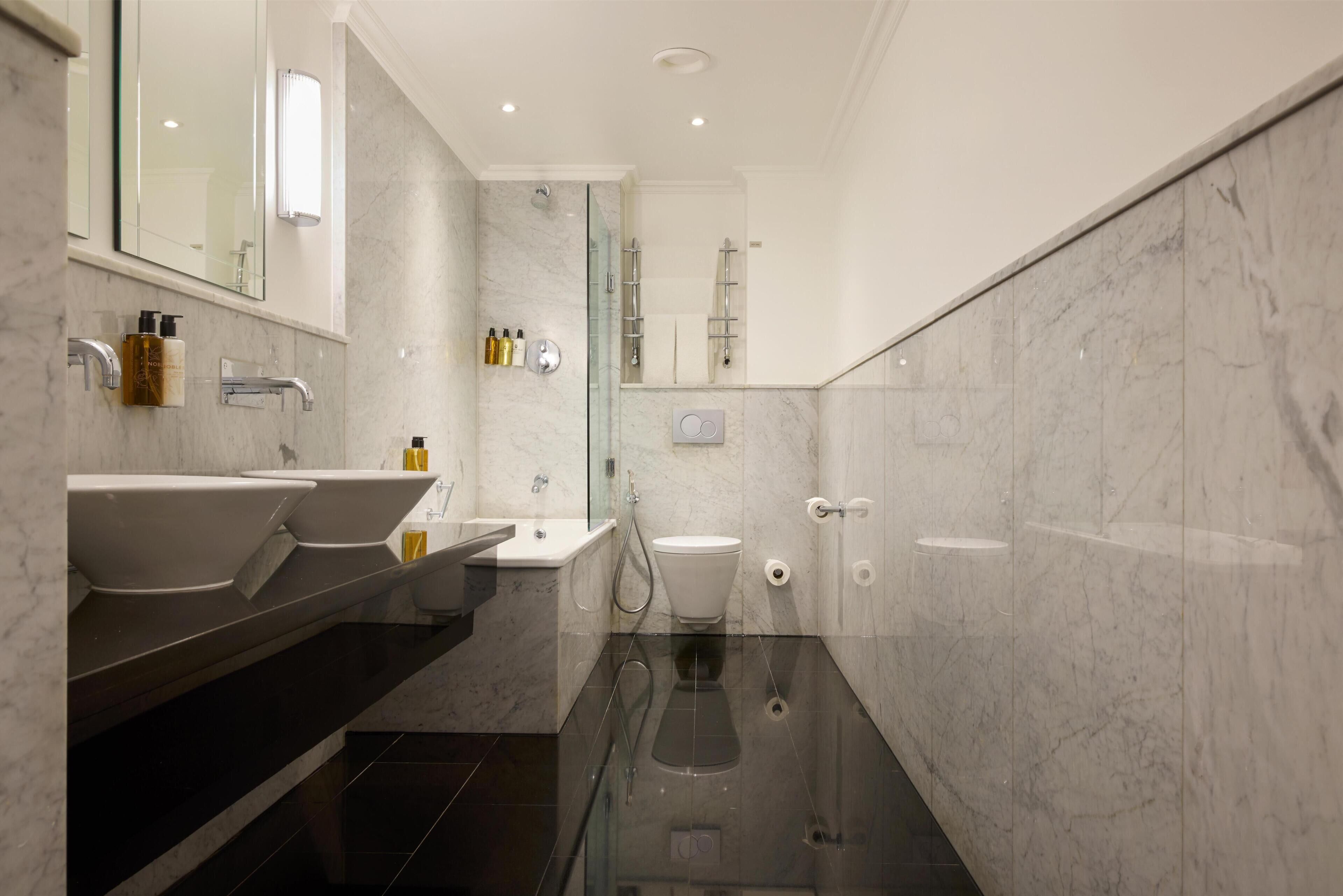 Et moderne badeværelse med to håndvaske, toilet og brusekabine med glasvægge.