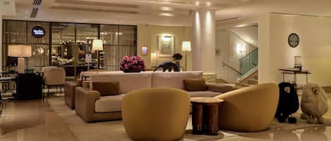 Un lobby moderno de hotel con un área de descanso, una recepción y vistas al área de la cocina.