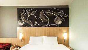 A hotel room with a bed, bedside lamps, a red suitcase, and a wall art piece. - ibis Chatellerault (Chatellerault)
