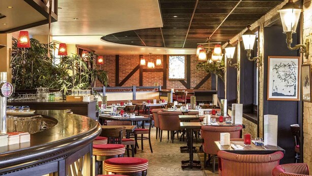 A restaurant interior with brick walls, wooden beams, and a bar area with stools. - ibis Chatellerault (Chatellerault)