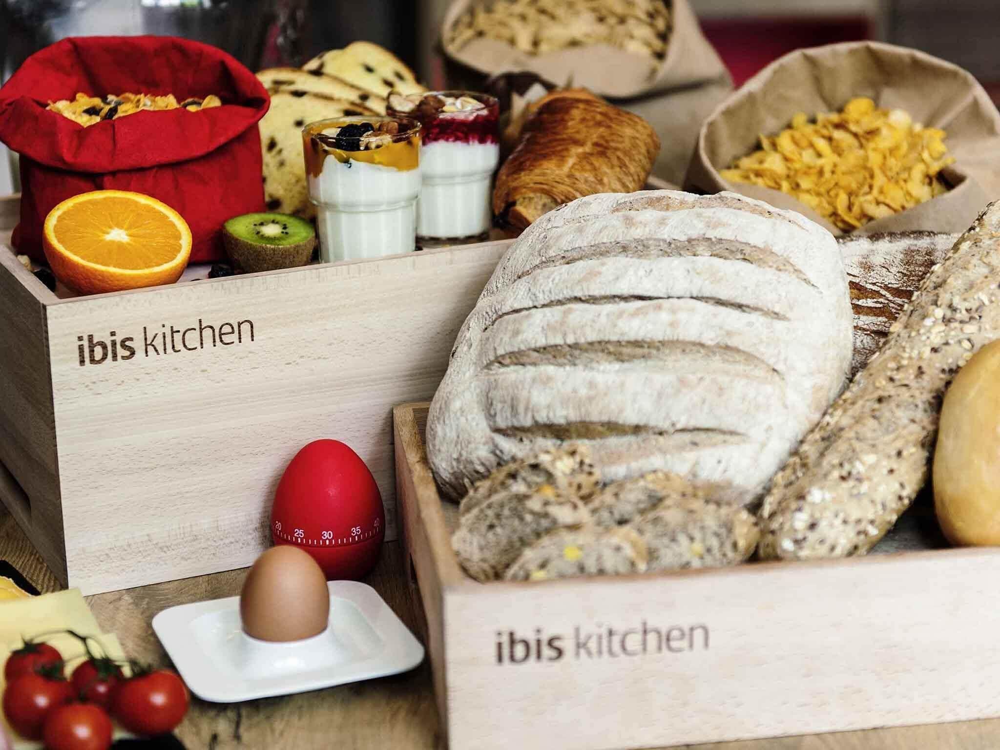 A wooden box labeled 'ibis kitchen' containing various food items like bread, eggs, and fruits.