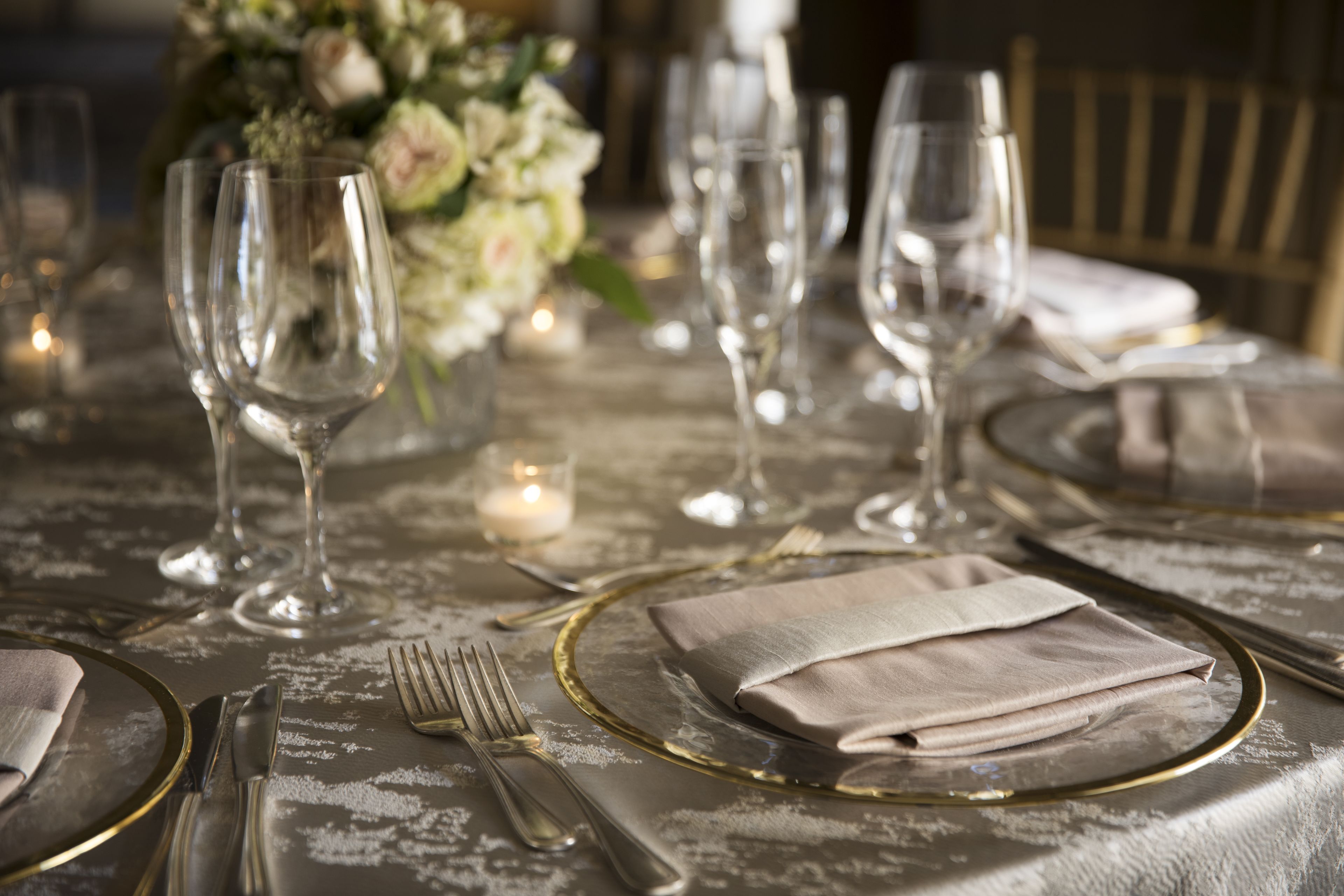 Een gedekte tafel voor een formeel diner, met helder glaswerk, gouden randen op de borden en gevouwen servetten.
