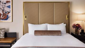 A hotel room with a large bed, a headboard, a bedside table with a lamp, a chair, and a painting on the wall.