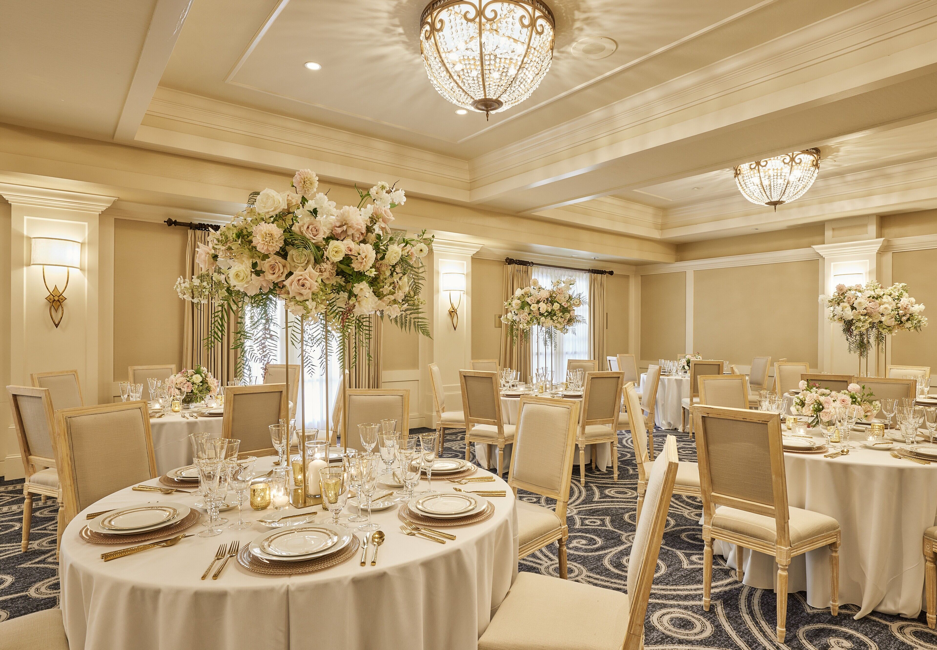 Un salón de banquetes con mesas redondas dispuestas para comer, con sillas de tono dorado y manteles blancos.