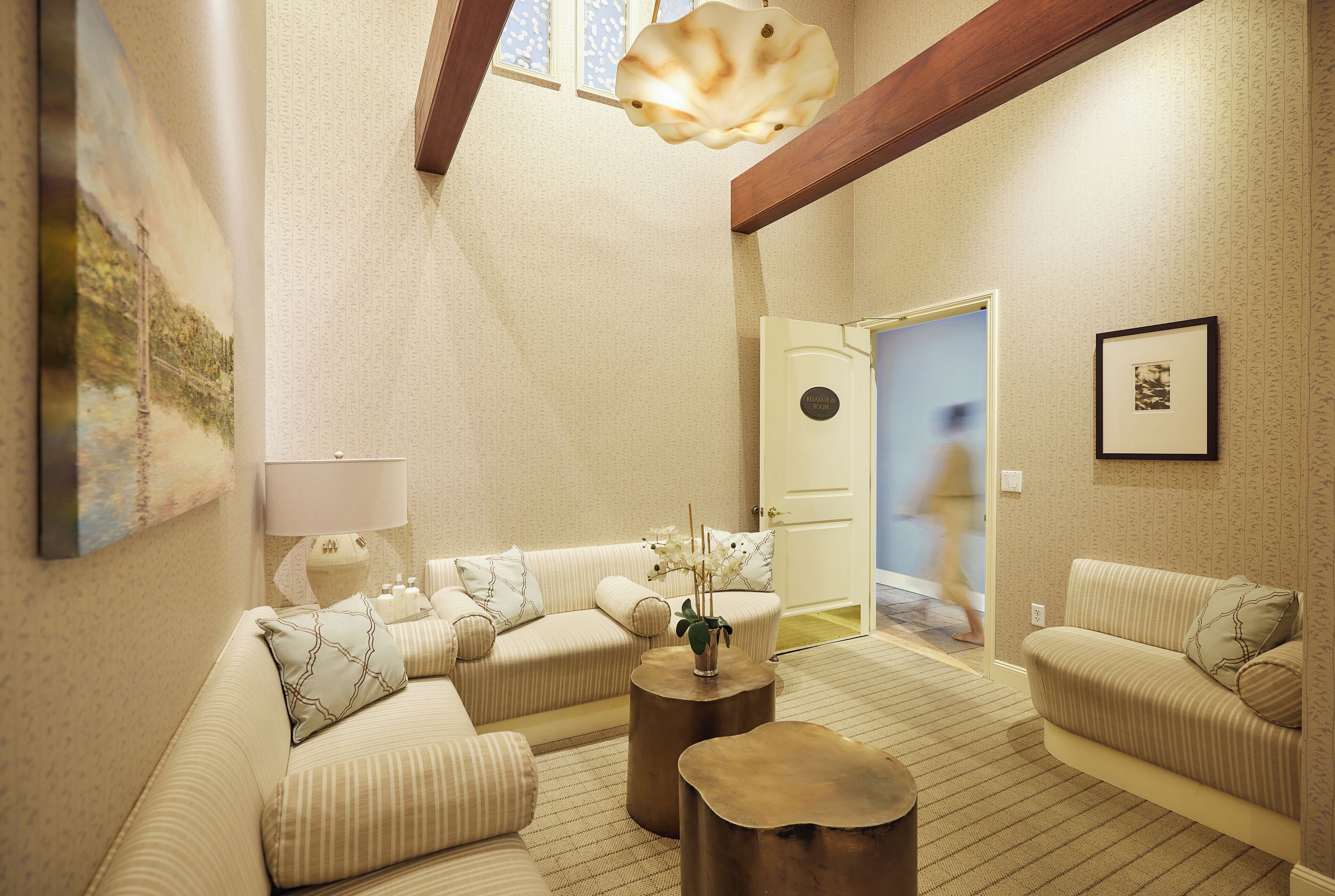 A well-lit living room with a sofa set, a coffee table, and a lamp. There is a door leading to another room.