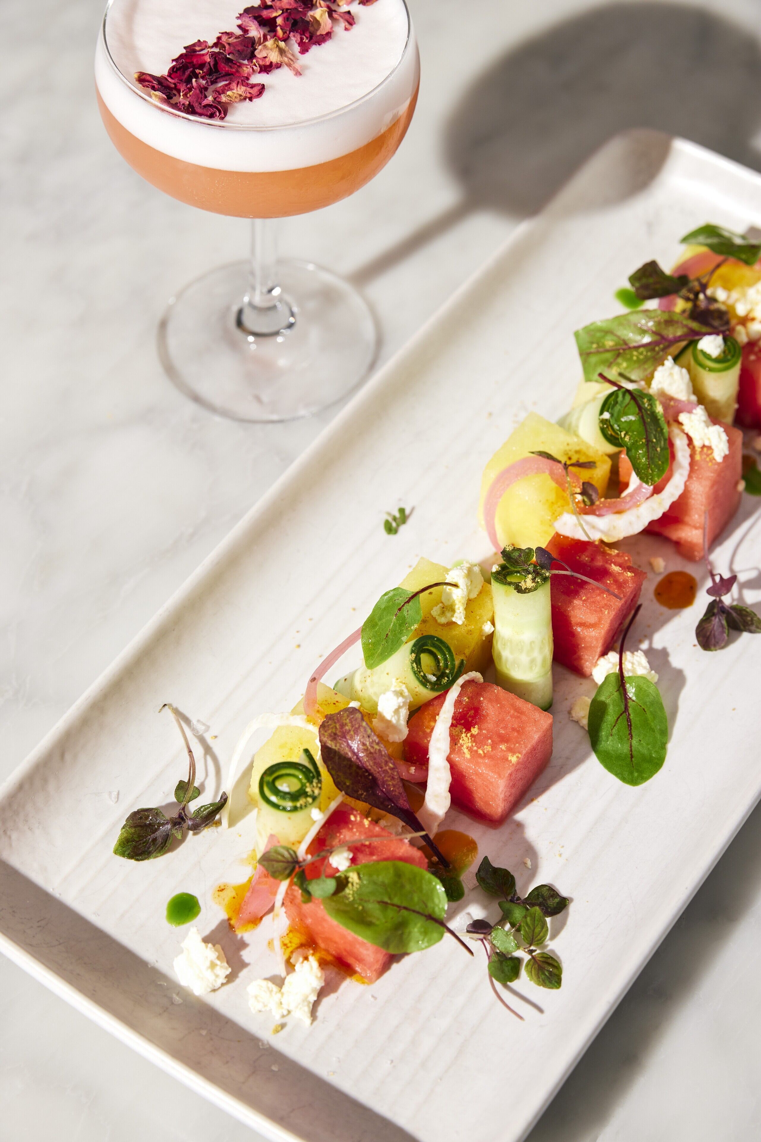 A white rectangular plate with a colorful salad and a cocktail glass.