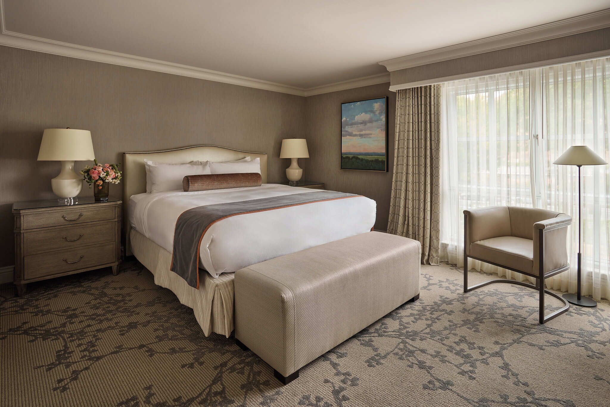 A hotel room with a large bed, two bedside tables with lamps, a chair, and a window with curtains.