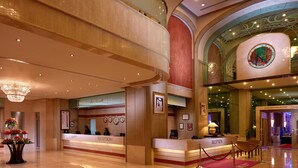 A hotel lobby with a reception desk, a chandelier, and a red carpet leading to the ballroom.
