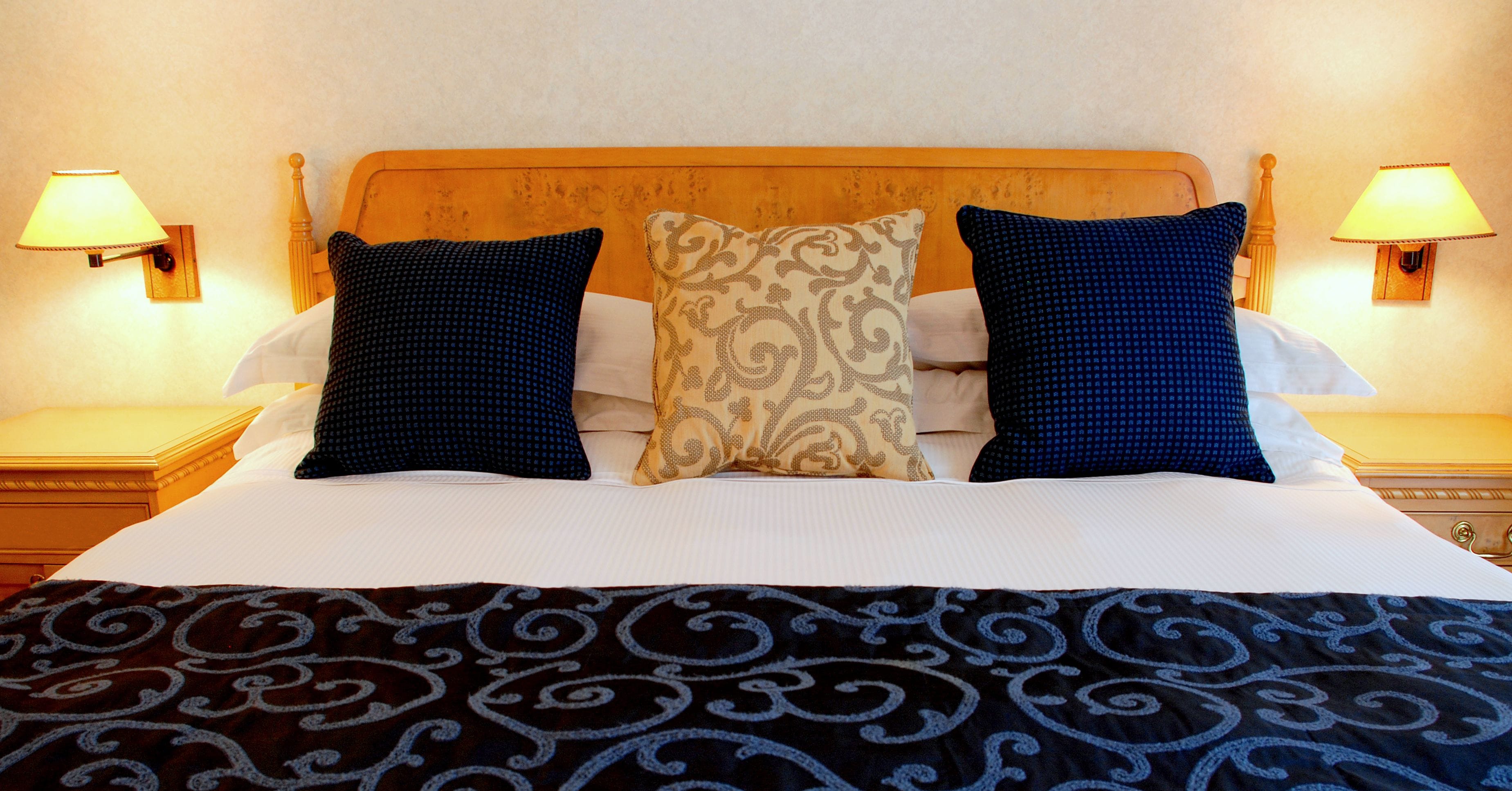 Een keurig opgemaakt bed met een bedsprei met patroon, twee kussens en een houten hoofdbord.