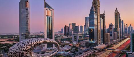 A modern cityscape with prominent skyscrapers and a unique spherical structure with Arabic script.