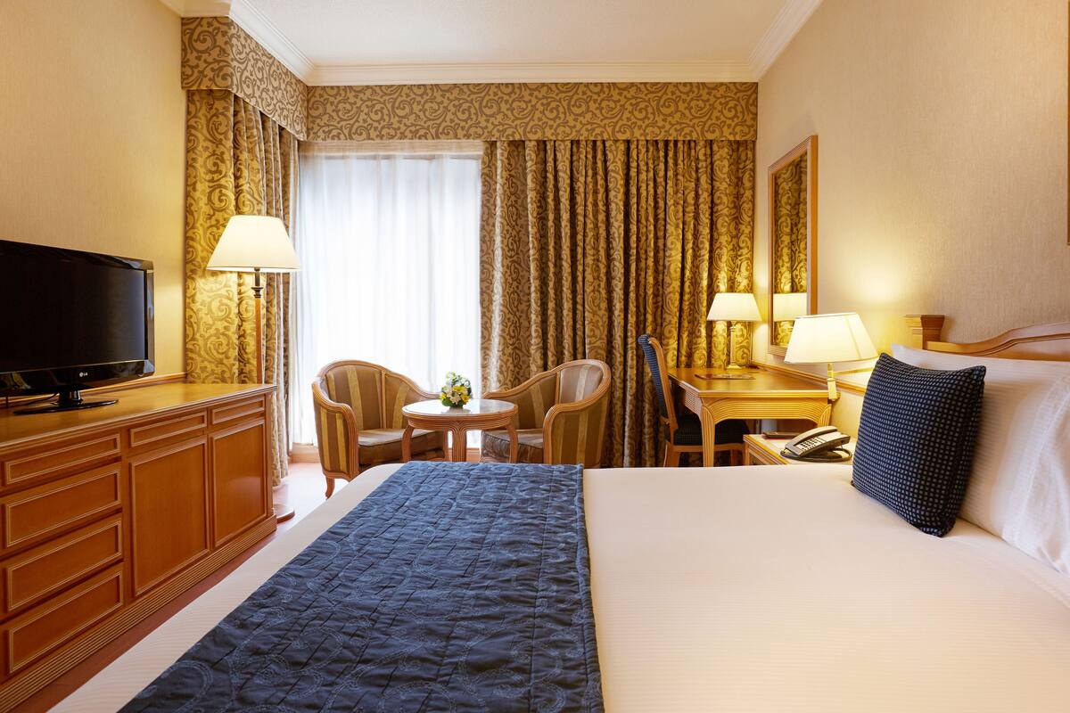 Hotelkamer met een bed, een televisie, een bureau met lamp, een stoel en een tafeltje met een vaas.