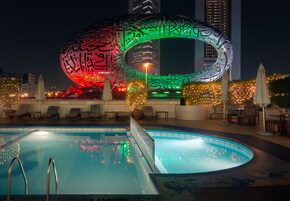 A swimming pool with a large illuminated arch structure in the background.