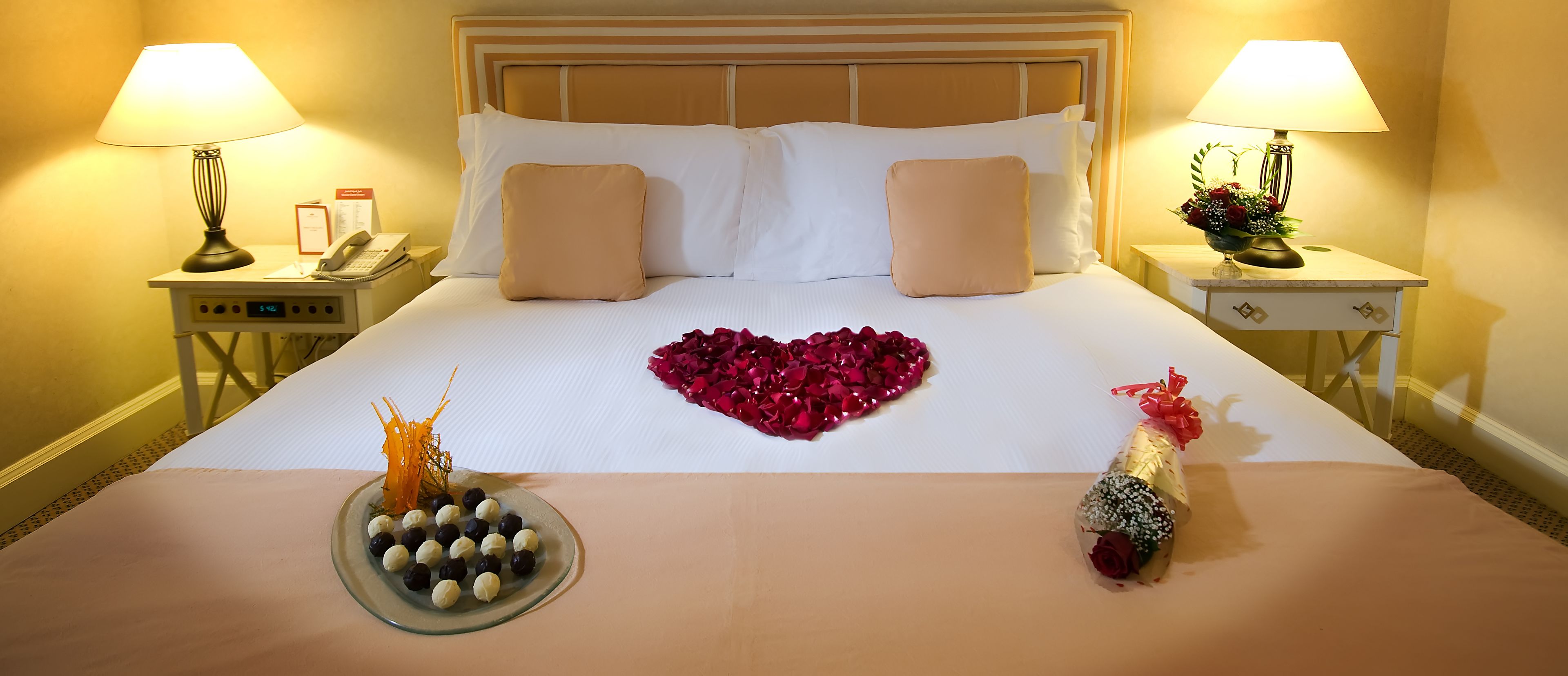A hotel room with a neatly made bed, two bedside tables with lamps, a telephone, and a small card on the left table.