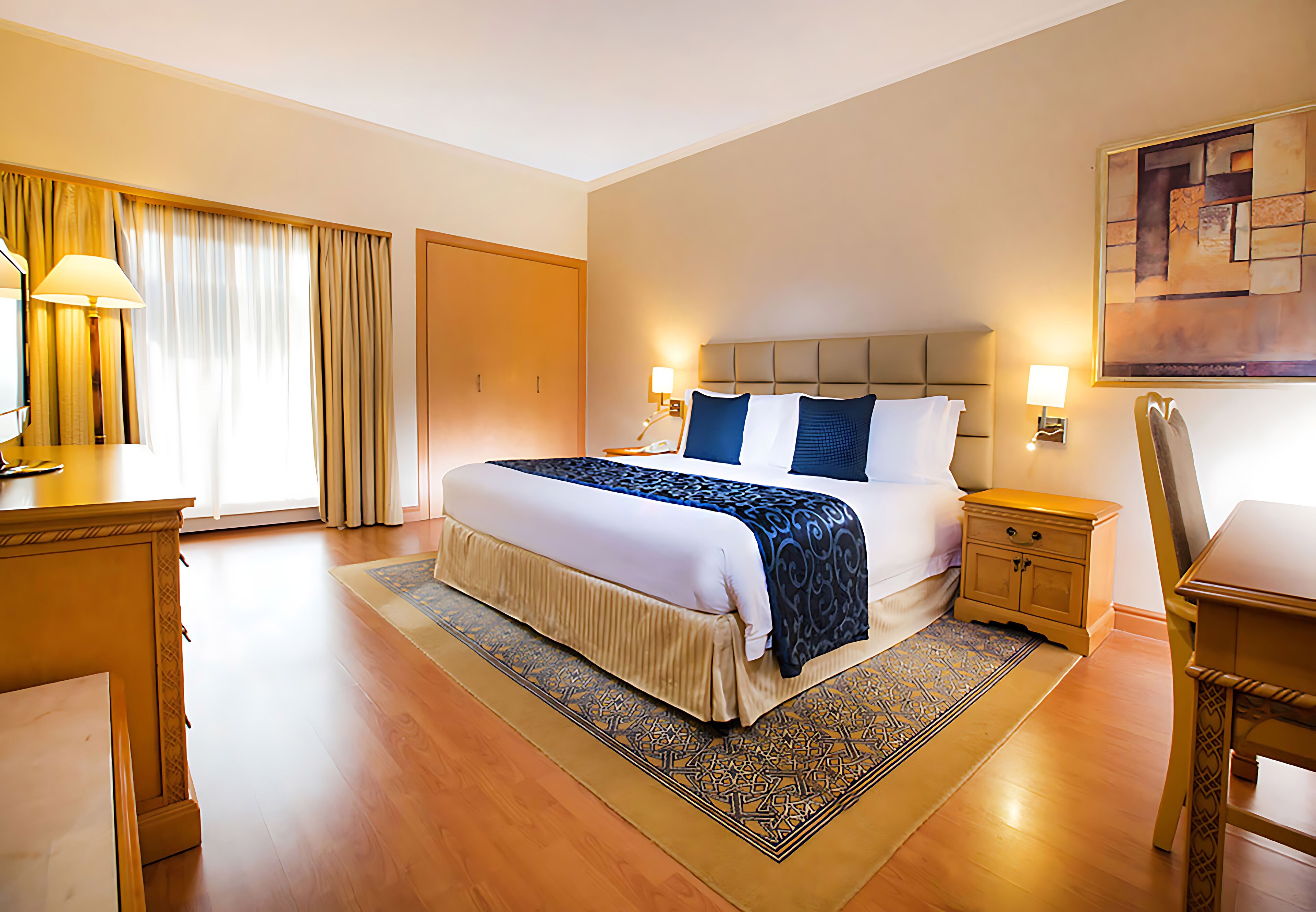 Una habitación de hotel con una cama grande, mesitas de noche, un escritorio y una silla.