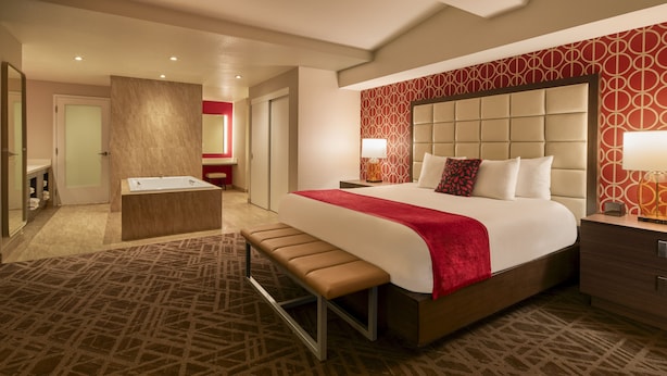 A hotel room with a large bed, a bench, a bedside table, a nightstand, and a bathroom with a bathtub and vanity. - Horseshoe Las Vegas (Las Vegas)