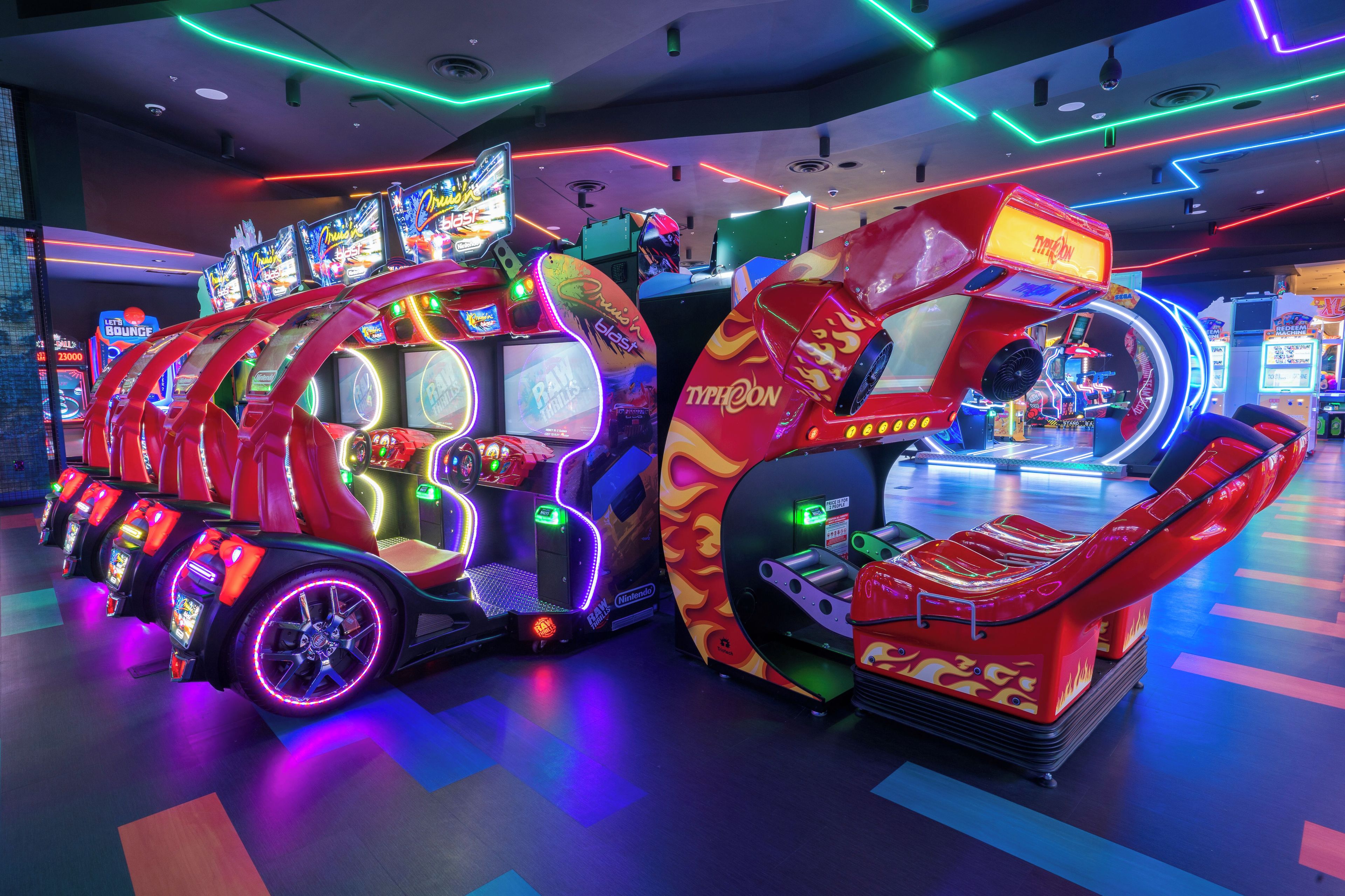 Una hilera de máquinas de videojuegos de arcade con luces de neón y una máquina de garra grande e iluminada.