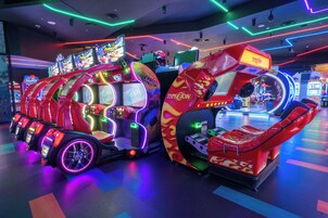 Una hilera de máquinas de videojuegos de arcade con luces de neón y una máquina de garra grande e iluminada.