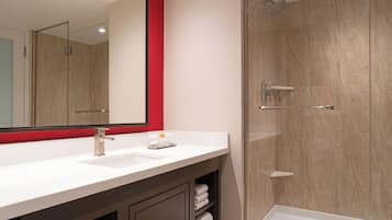 Un baño moderno con un lavamanos blanco, un espejo grande de marco rojo y una zona de ducha con paredes de vidrio.