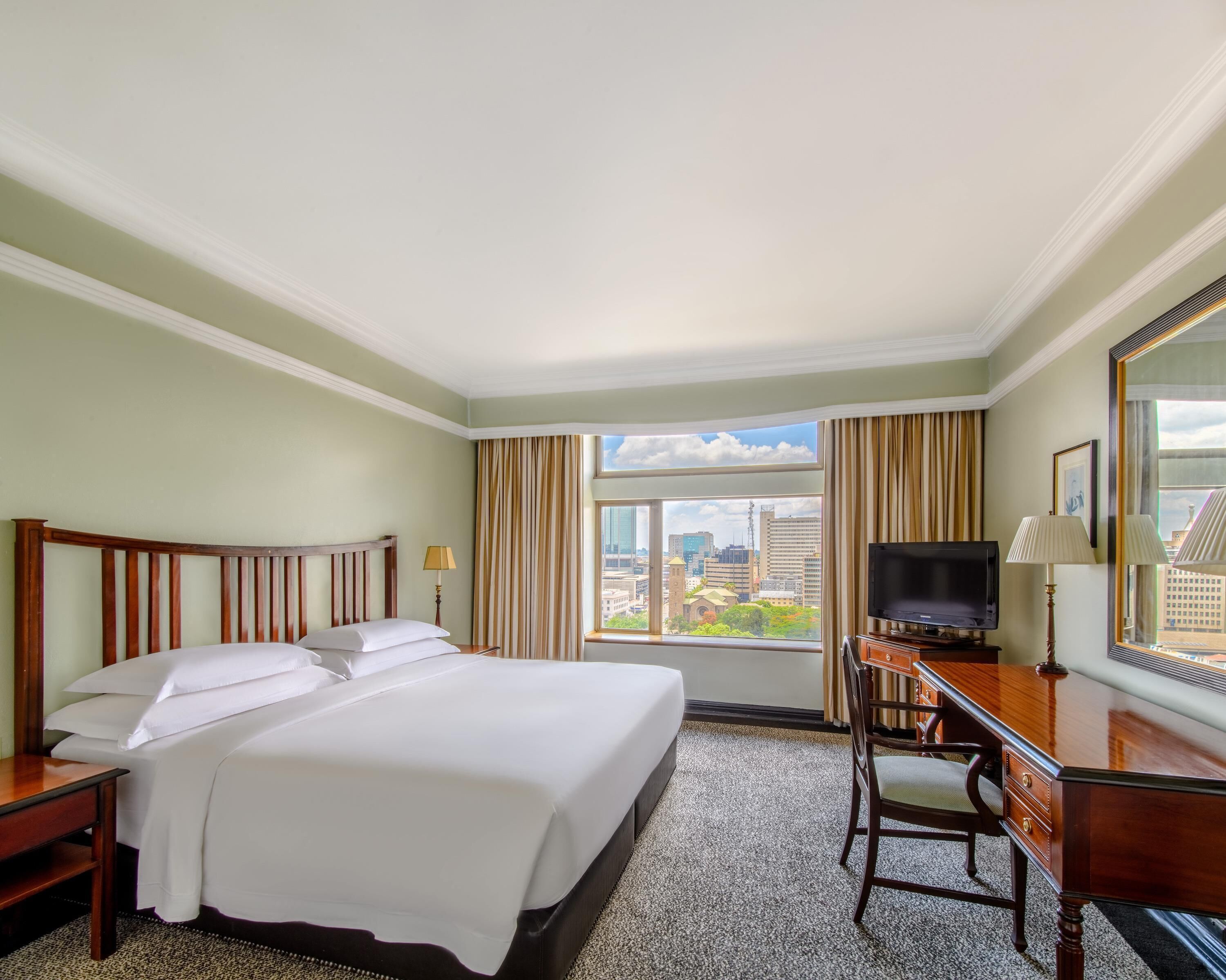 Habitación de hotel con una cama grande, un escritorio con televisor y vistas a la ciudad a través de la ventana.