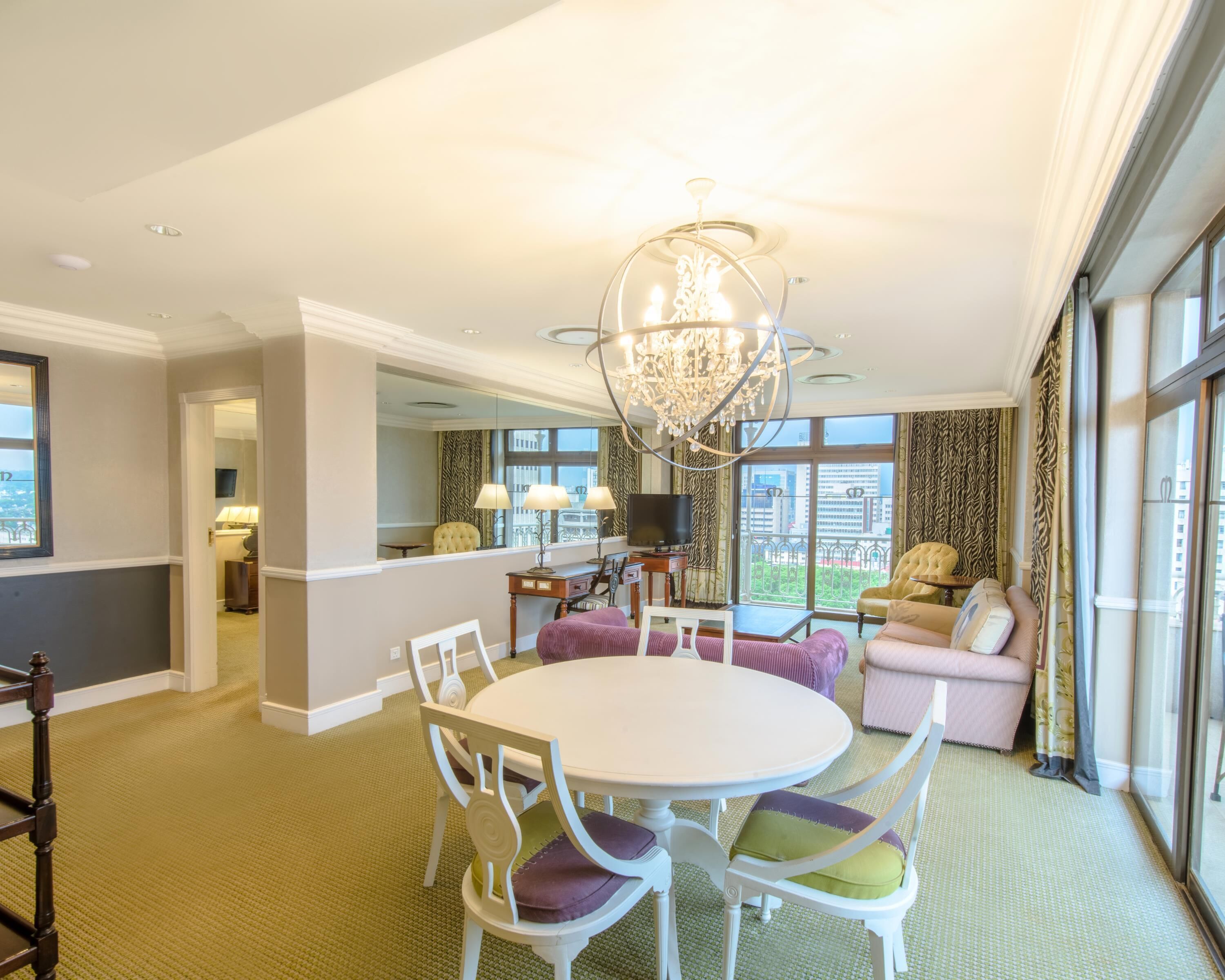 Quarto de hotel com área de refeições, lustre, grande janela com vista e televisão.