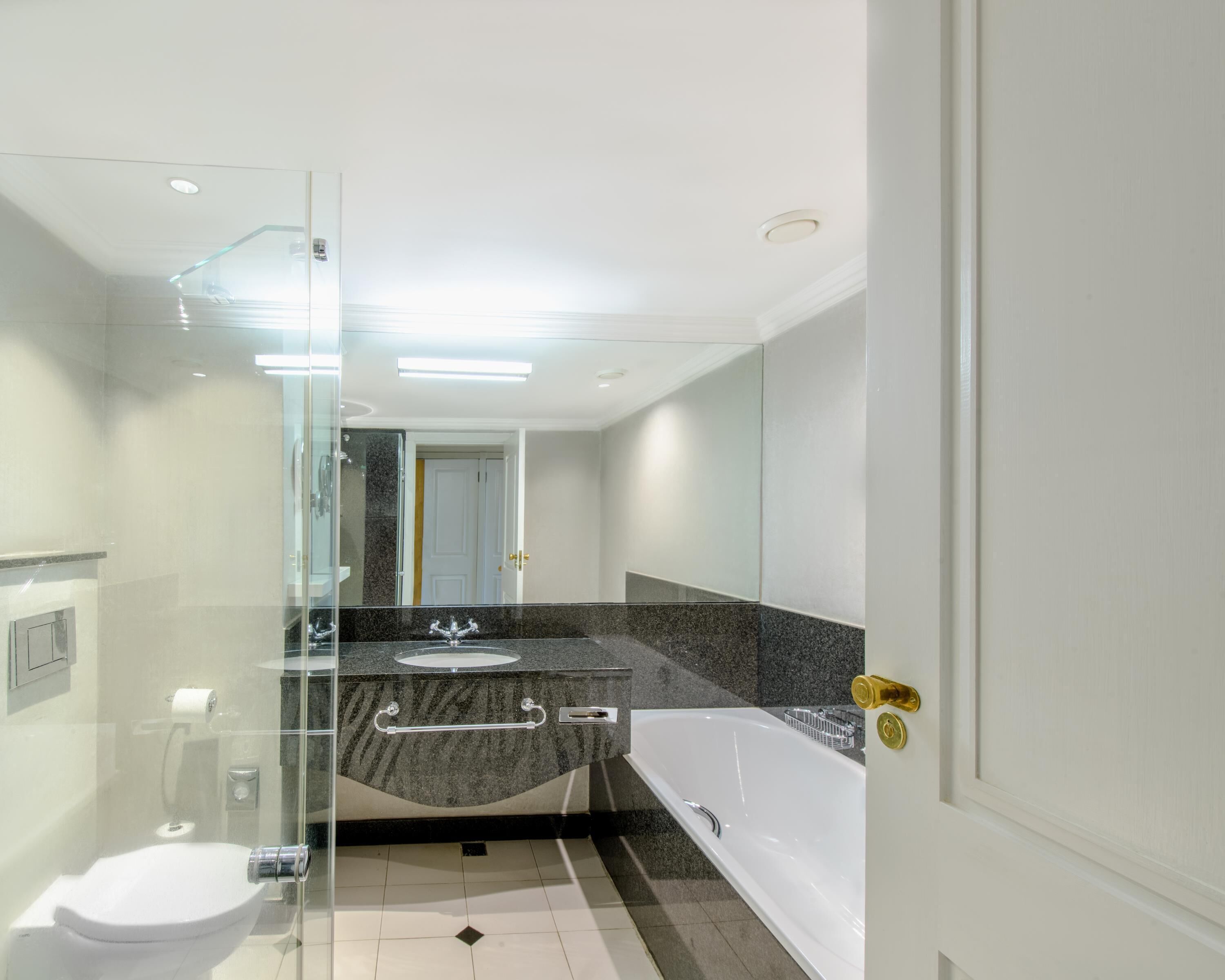 A modern bathroom with a glass shower enclosure, a white toilet, a granite countertop sink, and a white bathtub.
