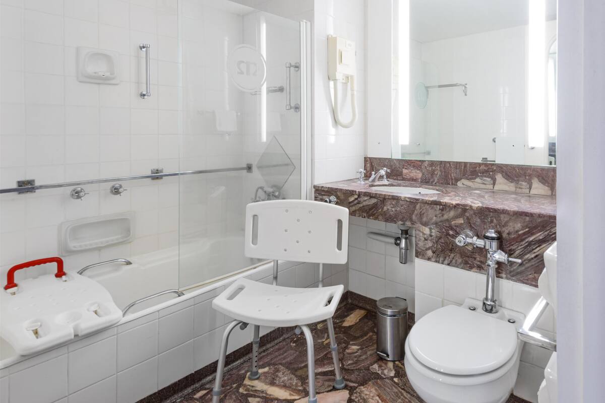 A modern bathroom with a glass shower enclosure, a white toilet, a marble sink vanity, and a wheelchair-accessible bench.