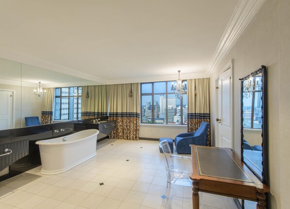 A spacious bathroom with a bathtub, a large mirror, and a window with curtains. - Hyatt Regency Harare The Meikles (Harare)