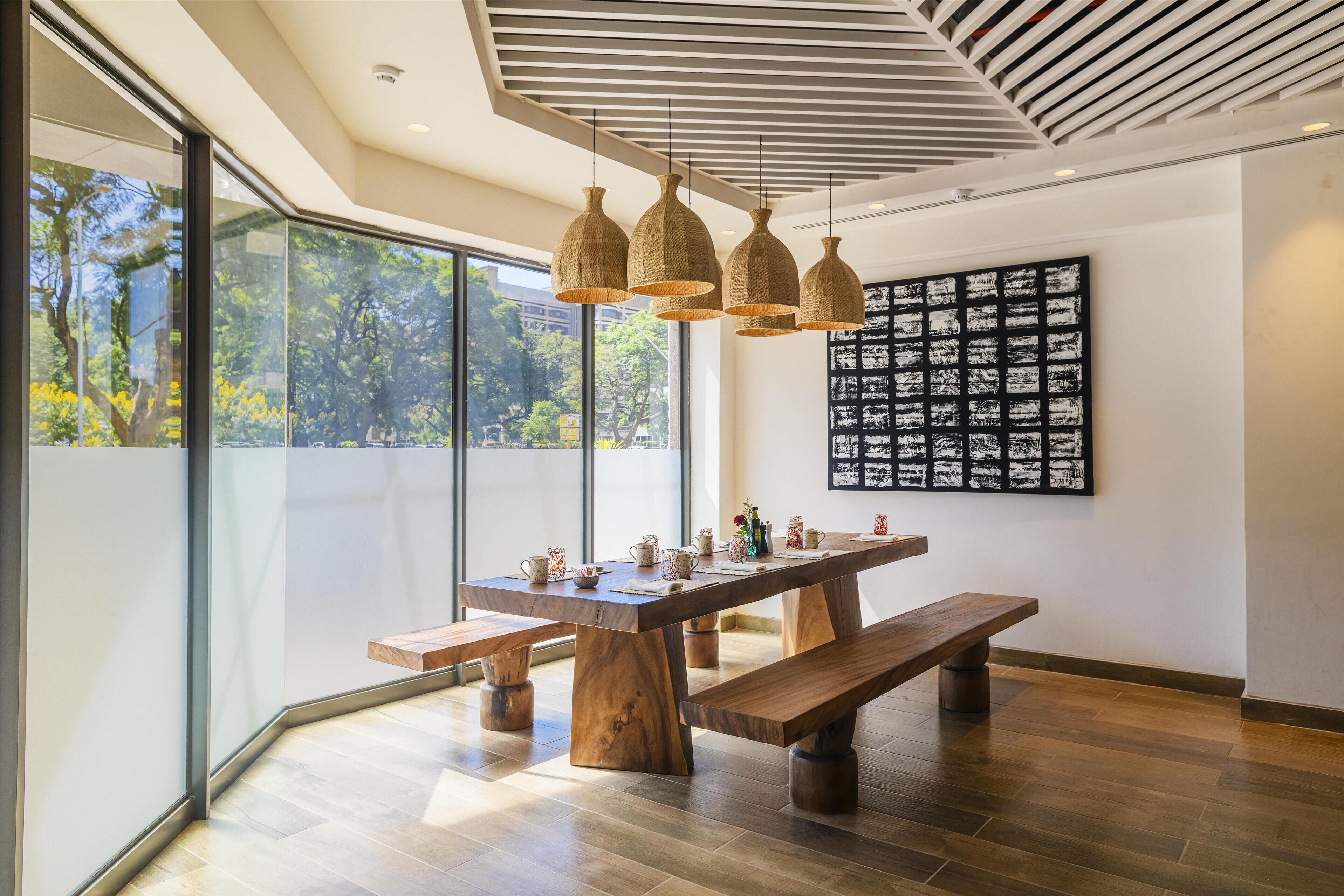 Un comedor moderno con una gran mesa de madera, bancos y lámparas colgantes.