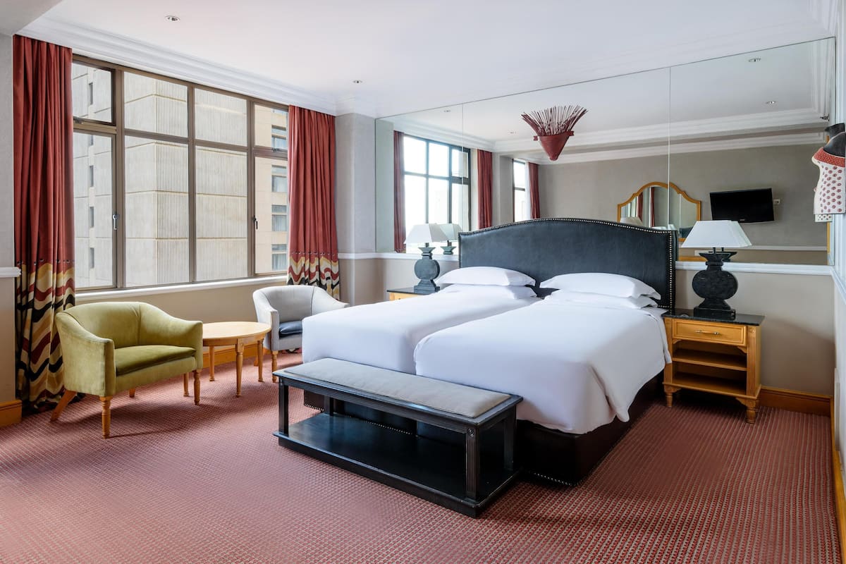 A hotel room with a large bed, a chair, a small table, and a bench.