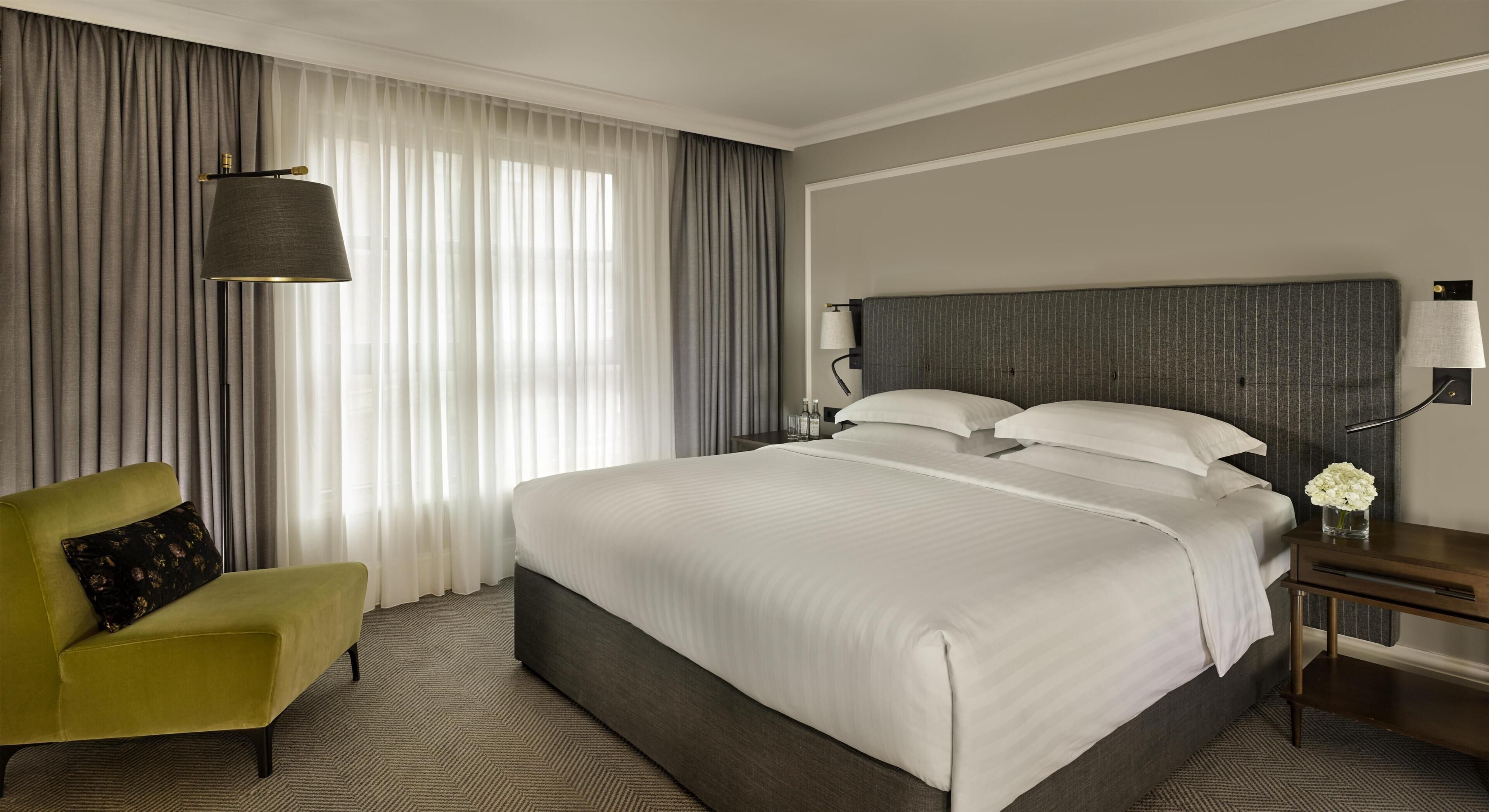 Une chambre d’hôtel avec un grand lit, une chaise, une table de chevet et une lampe.