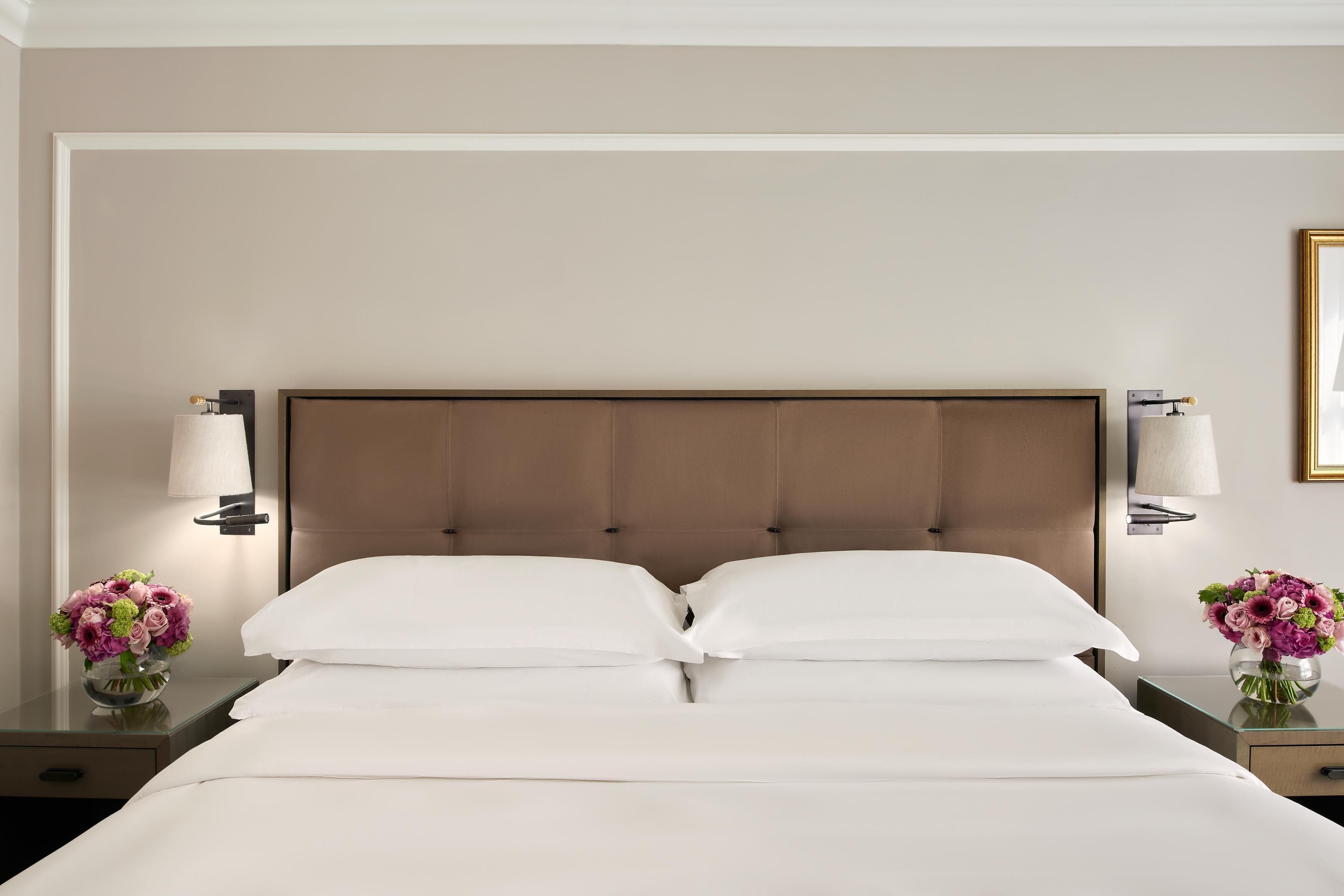 Une chambre d’hôtel avec un grand lit, deux tables de chevet et des lampes fixées au mur.