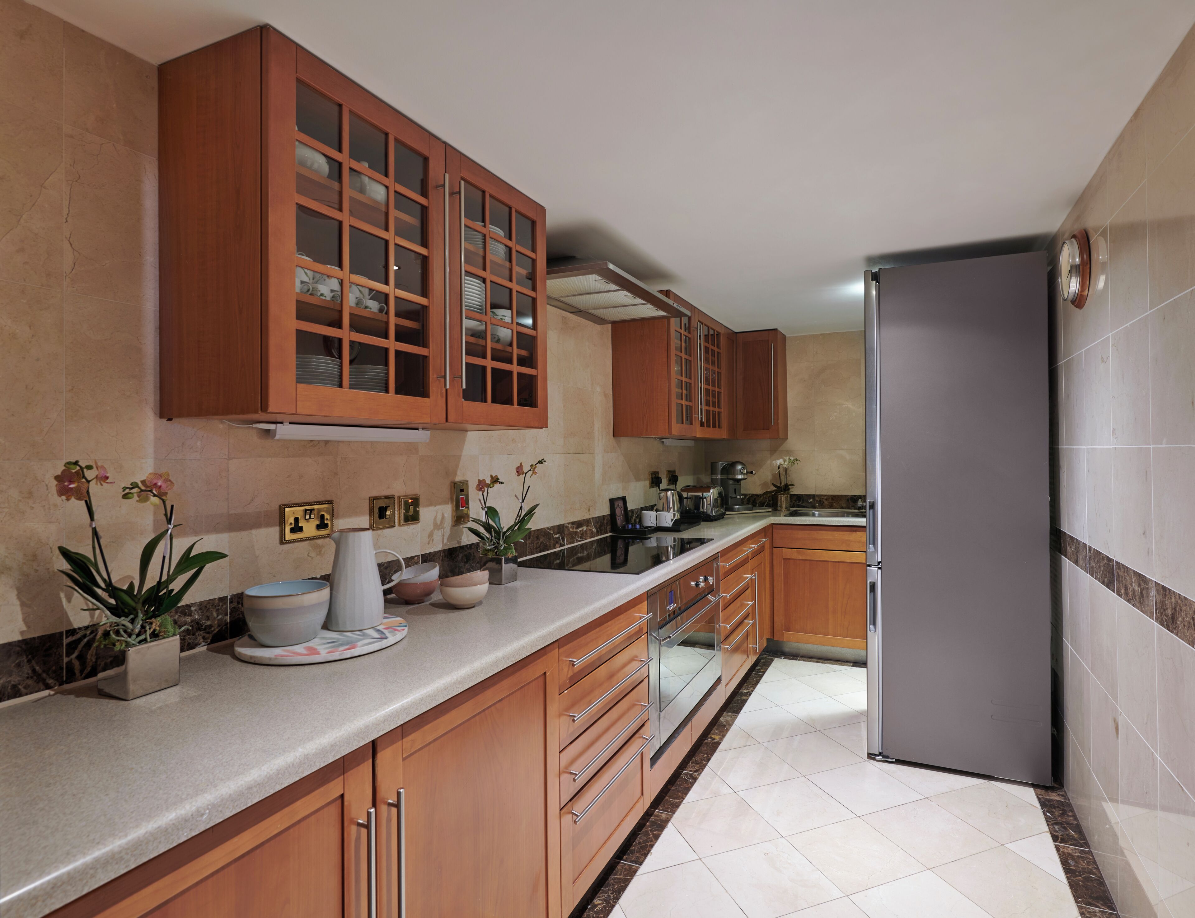 Una cocina con armarios de madera, refrigerador de acero inoxidable y encimera de mármol.